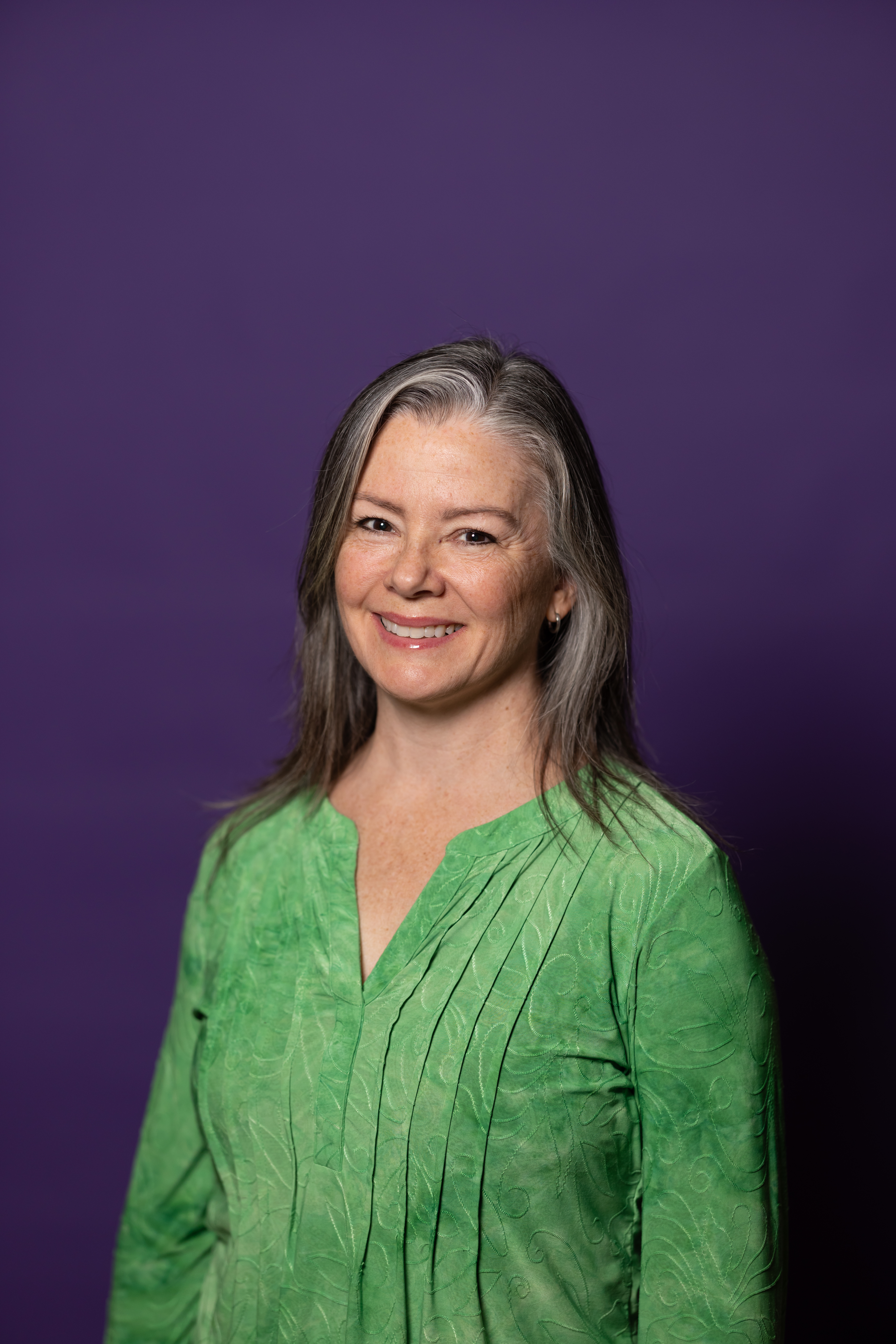 Amy smiling at the camera with a green shirt on and a purple background