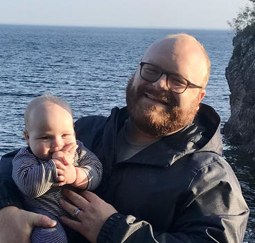 man holding baby with ocean in the background